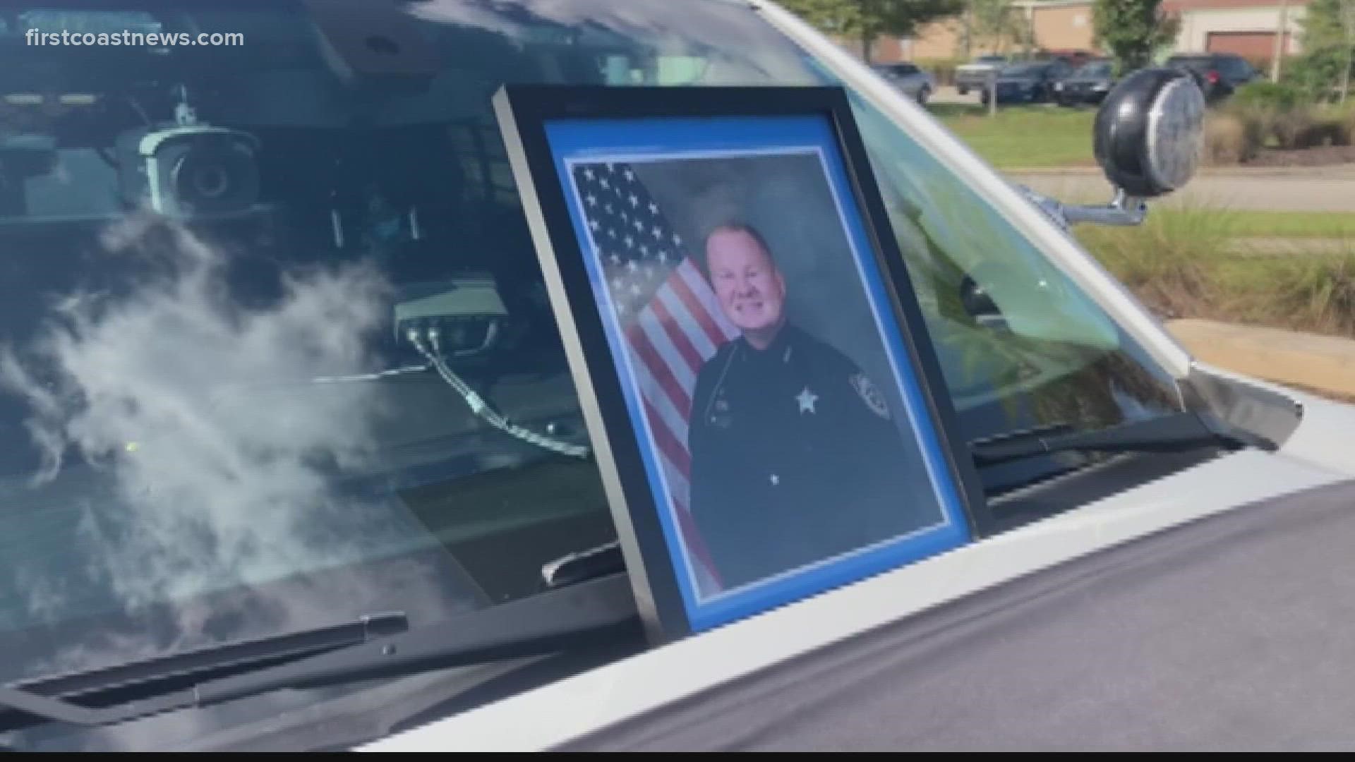 The memorial is a squad vehicle with a picture of Deputy Moyers on the windshield, a blue wreath on the grill and a black ribbon over the hood."